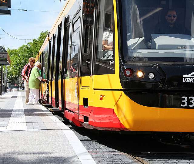 Zwei Frauen steigen in die Straßenbahn ein, eine von ihnen steigt mit einer Gehhilfe ein.
