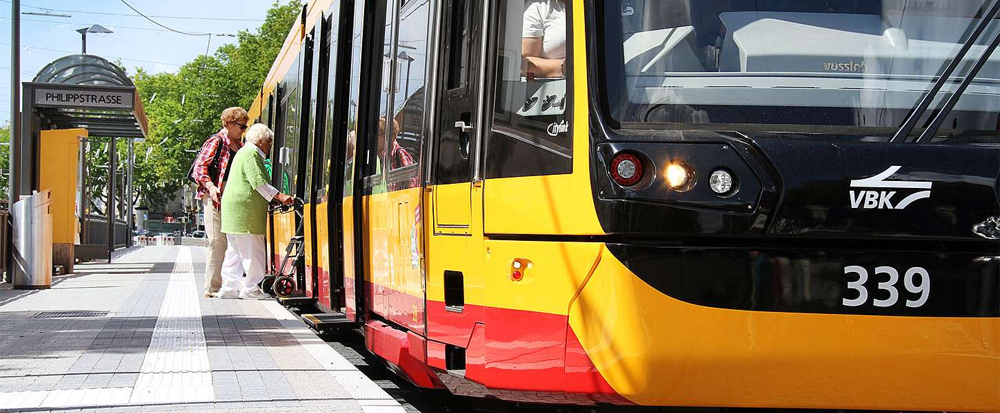 Zwei Frauen steigen in die Straßenbahn ein, eine von ihnen steigt mit einer Gehhilfe ein.