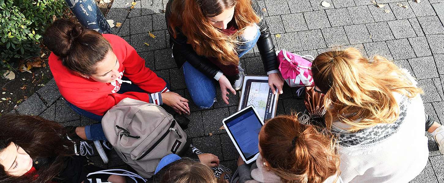 Sechs Mädchen sitzen auf dem Boden in einem Kreis und schauen auf zwei Tablets